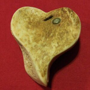 a human hip bone carved into the shape of a heart this heart fits into the palm of your hand. The heart has a 22 bullet at the top of the right hand side along with an old staple jammed into the bone